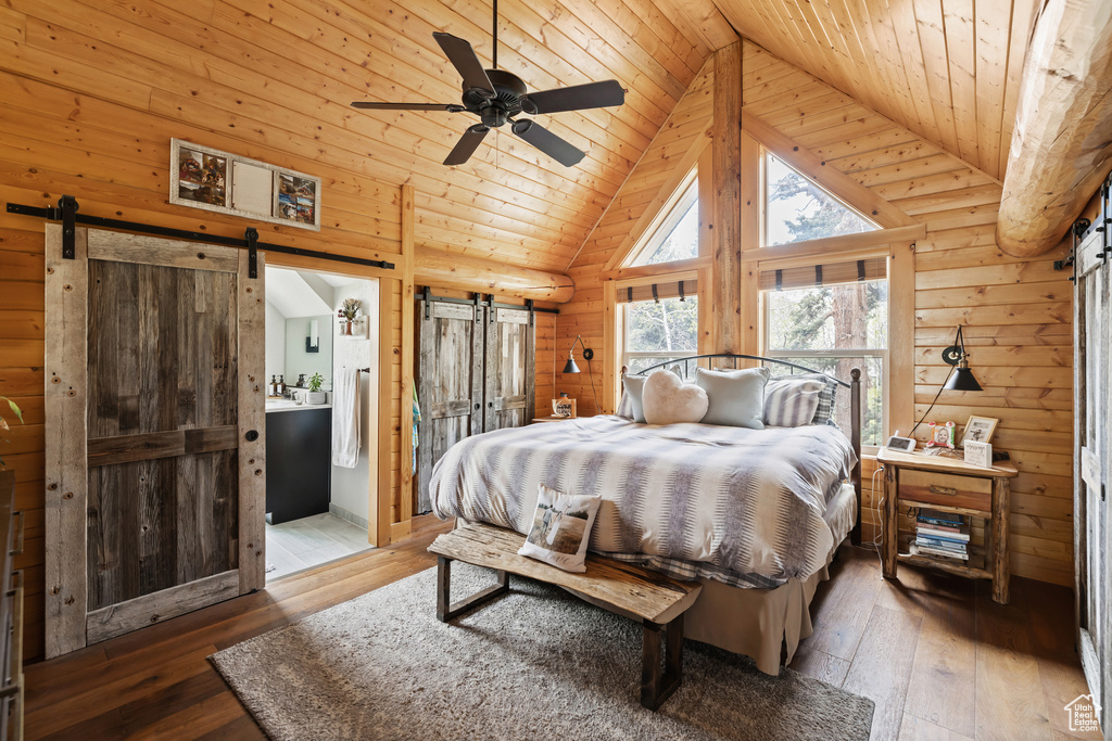 Bedroom with a barn door, wooden ceiling, hardwood / wood-style flooring, high vaulted ceiling, and log walls