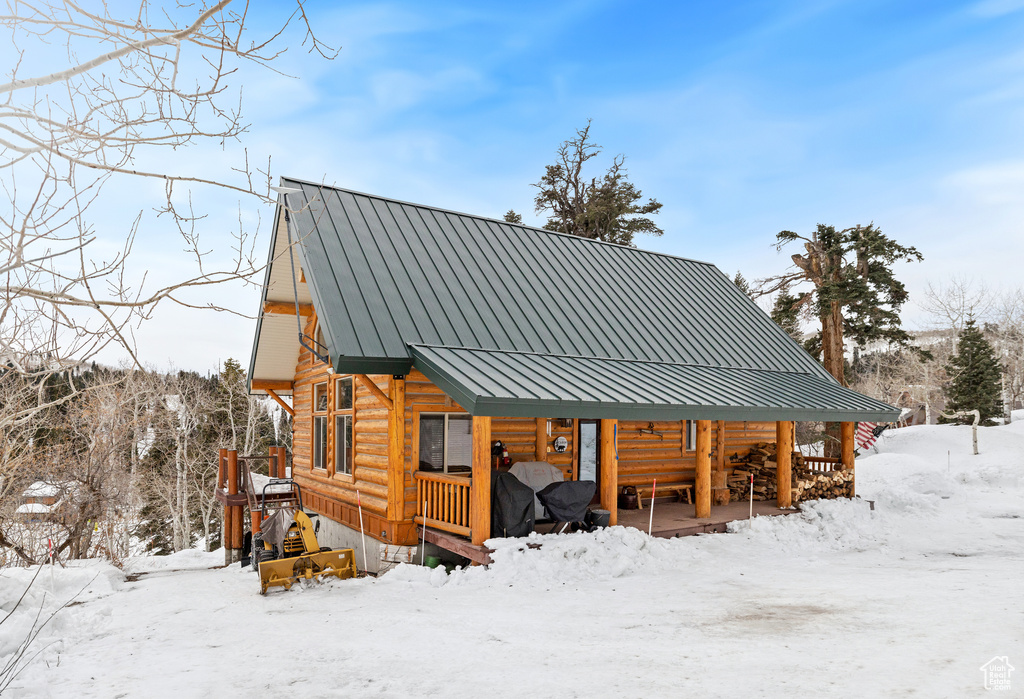 Snow covered rear of property with log siding, a porch, metal roof, and a standing seam roof