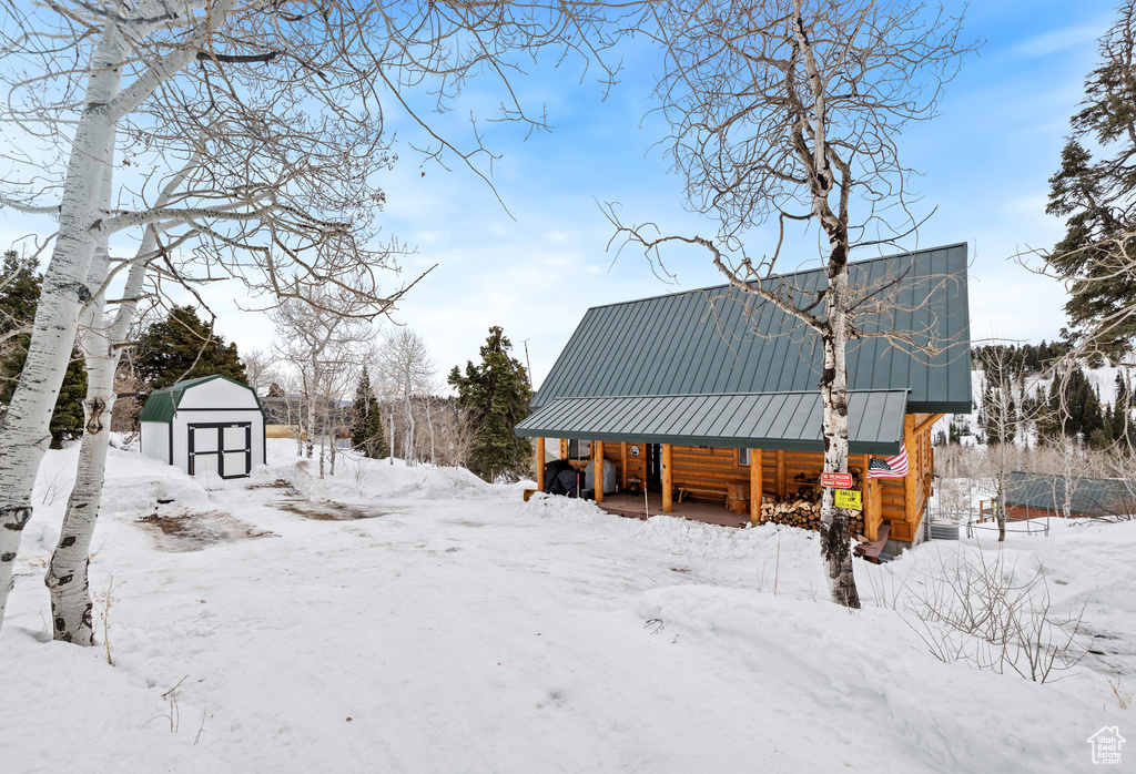 Yard layered in snow featuring a storage unit, an outdoor structure, and covered porch