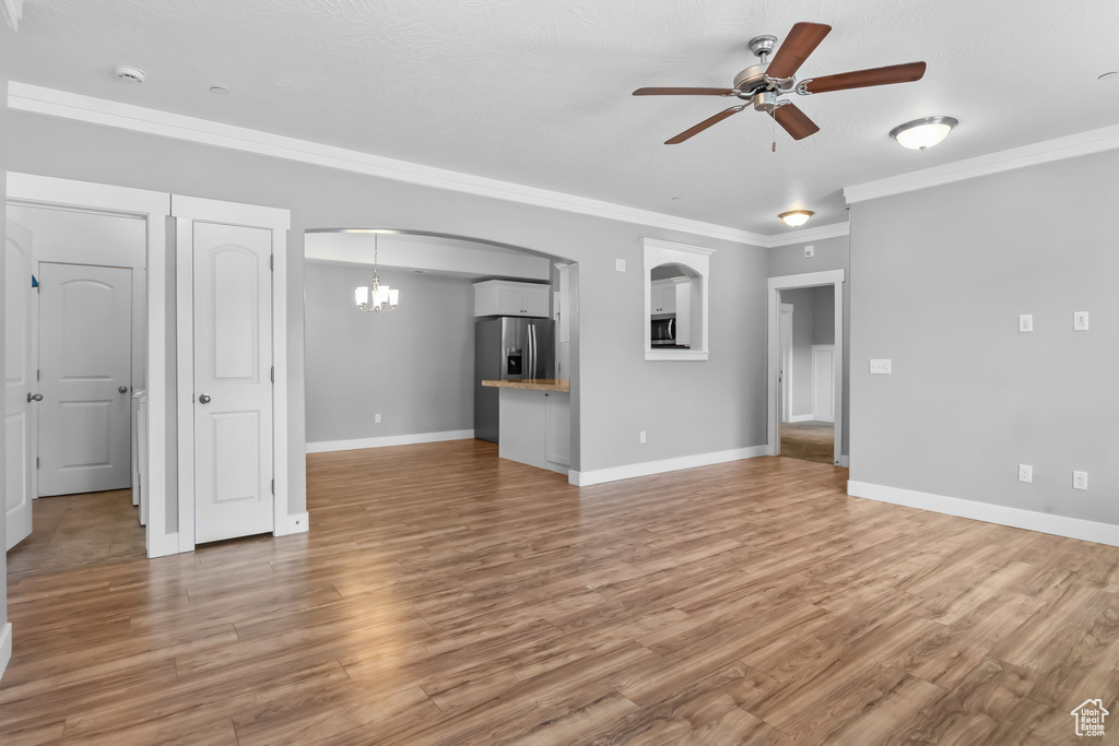 Unfurnished living room featuring crown molding, ceiling fan with notable chandelier, baseboards, and light wood-style floors
