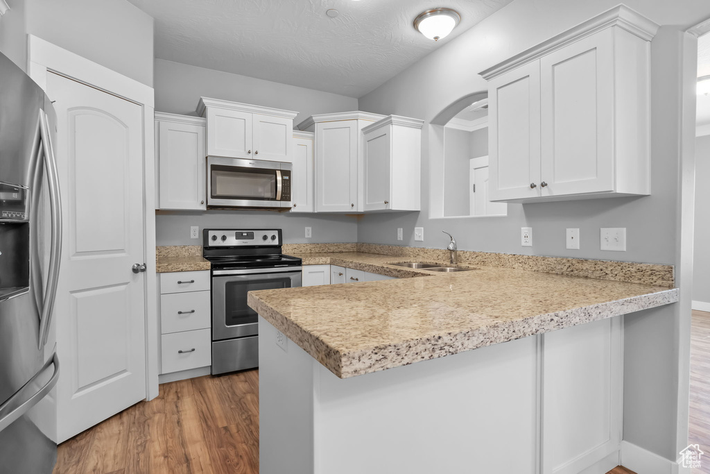 Kitchen with a peninsula, appliances with stainless steel finishes, a sink, and wood finished floors
