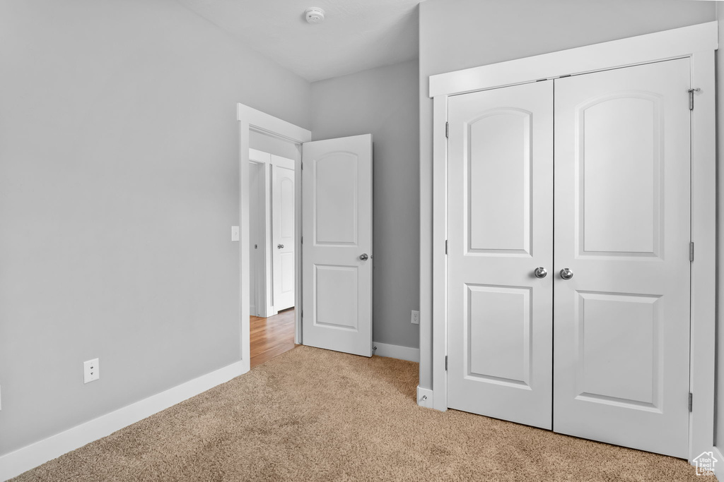Unfurnished bedroom with light colored carpet, a closet, and baseboards