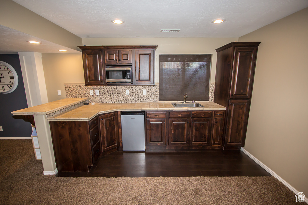 Kitchen with a peninsula, dishwashing machine, a sink, stainless steel microwave, and light countertops