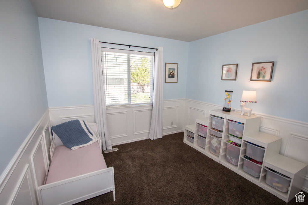 Living area featuring wainscoting, dark colored carpet, and a decorative wall