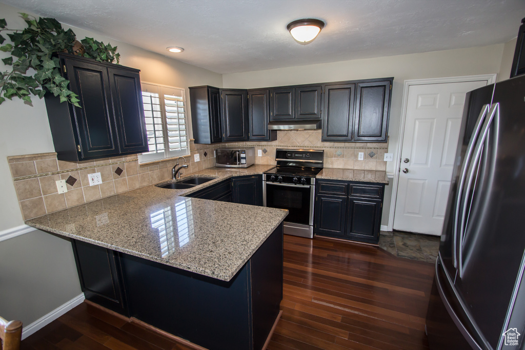 Kitchen featuring under cabinet range hood, a sink, a peninsula, appliances with stainless steel finishes, and dark wood-style floors