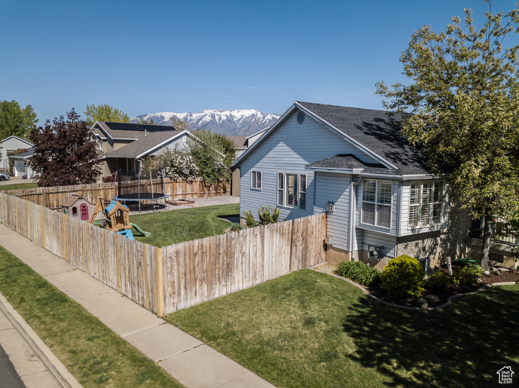 View of front of property with a mountain view, a trampoline, a front yard, roof with shingles, and a fenced backyard