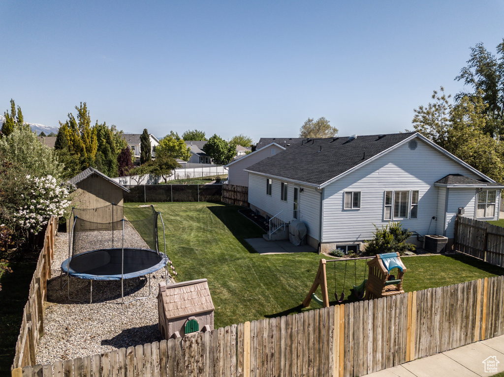 Back of property featuring a yard, a trampoline, roof with shingles, and a fenced backyard