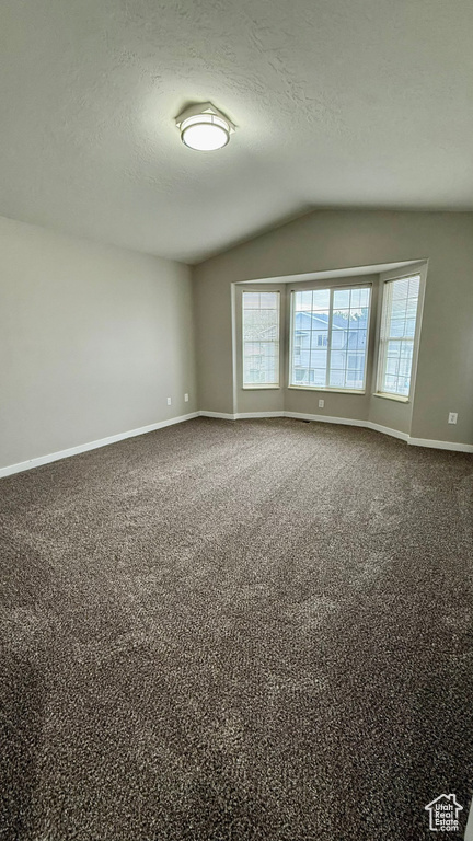 Spare room featuring lofted ceiling, baseboards, a textured ceiling, and dark colored carpet
