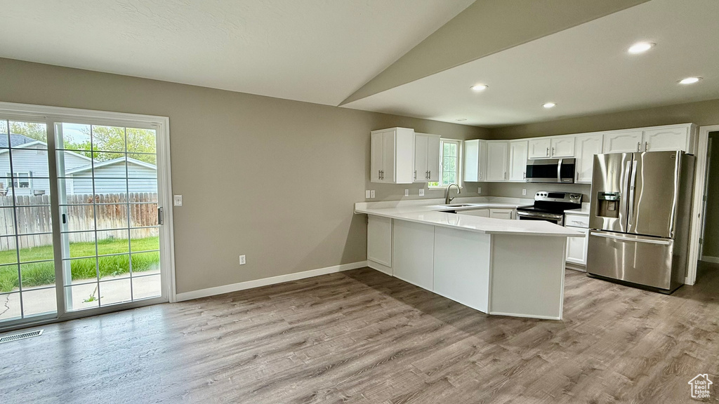 Kitchen featuring appliances with stainless steel finishes, healthy amount of natural light, a peninsula, vaulted ceiling, and a sink