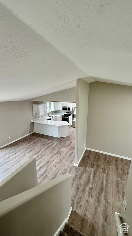 Unfurnished living room with lofted ceiling, wood finished floors, a textured ceiling, baseboards, and a sink