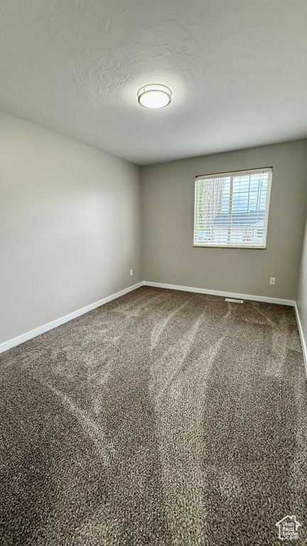Unfurnished room with baseboards, a textured ceiling, and dark carpet