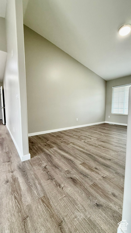 Empty room featuring vaulted ceiling, wood finished floors, and baseboards