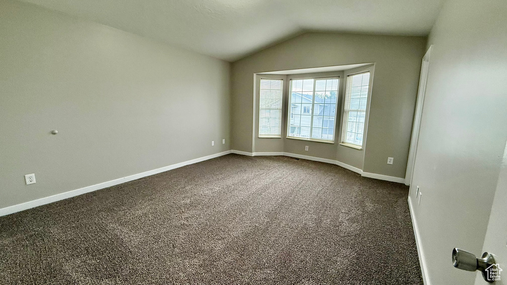 Spare room featuring vaulted ceiling, dark colored carpet, and baseboards