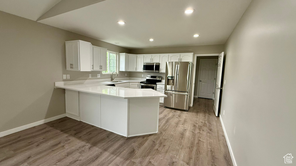 Kitchen with appliances with stainless steel finishes, a peninsula, a sink, baseboards, and light wood-style flooring