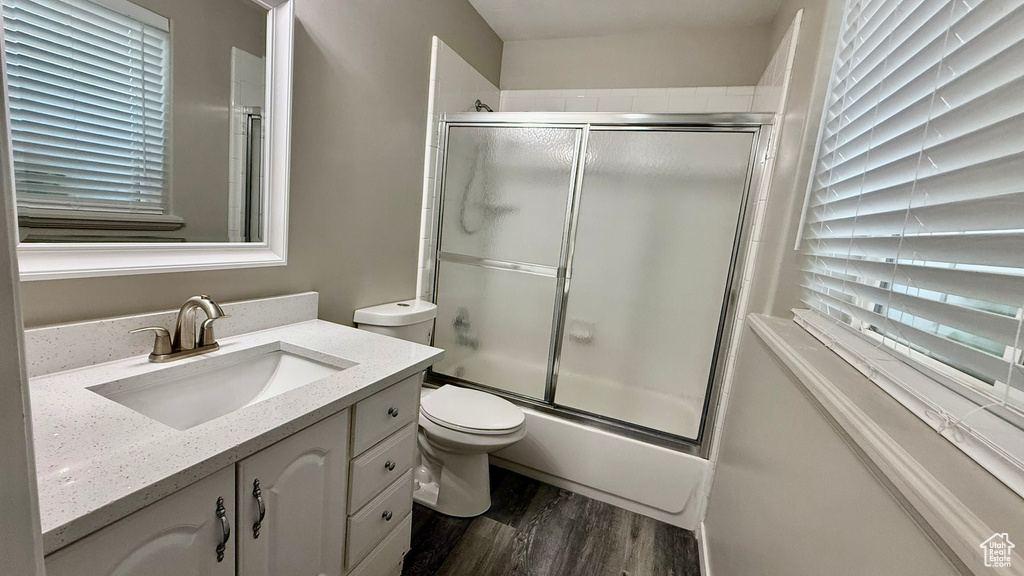 Bathroom with wood finished floors, bath / shower combo with glass door, healthy amount of natural light, and vanity