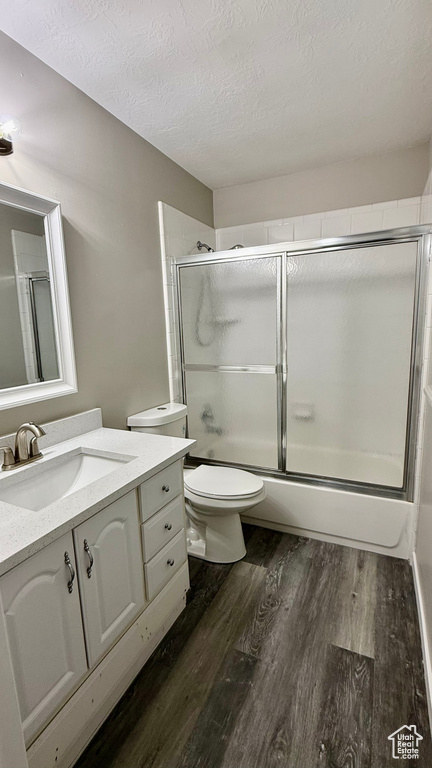 Full bathroom with a textured ceiling, wood finished floors, enclosed tub / shower combo, toilet, and vanity