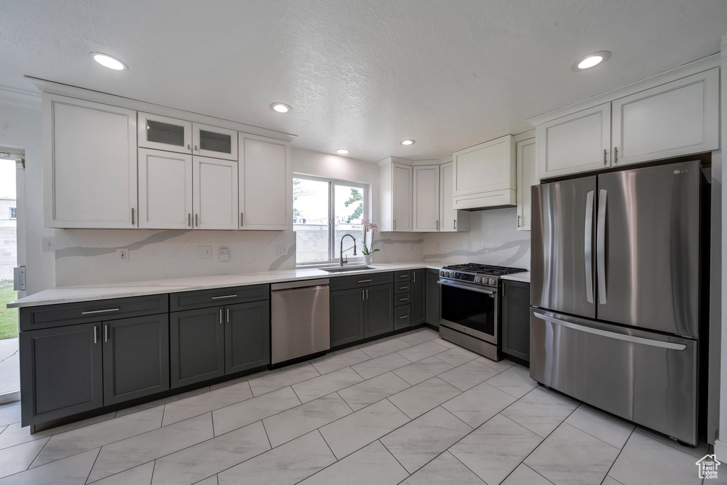 Kitchen with appliances with stainless steel finishes, a sink, light countertops, white cabinetry, and decorative backsplash