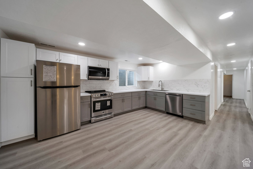Kitchen with appliances with stainless steel finishes, gray cabinetry, light wood-style floors, light countertops, and recessed lighting