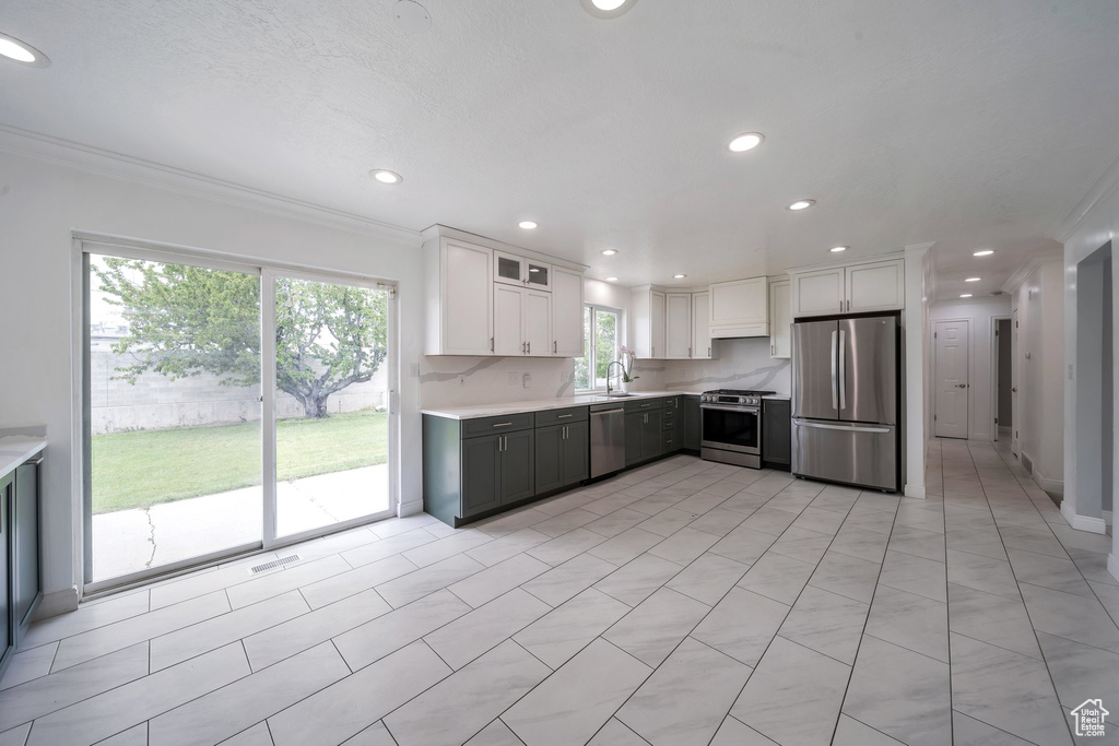 Kitchen with appliances with stainless steel finishes, light countertops, white cabinets, recessed lighting, and crown molding