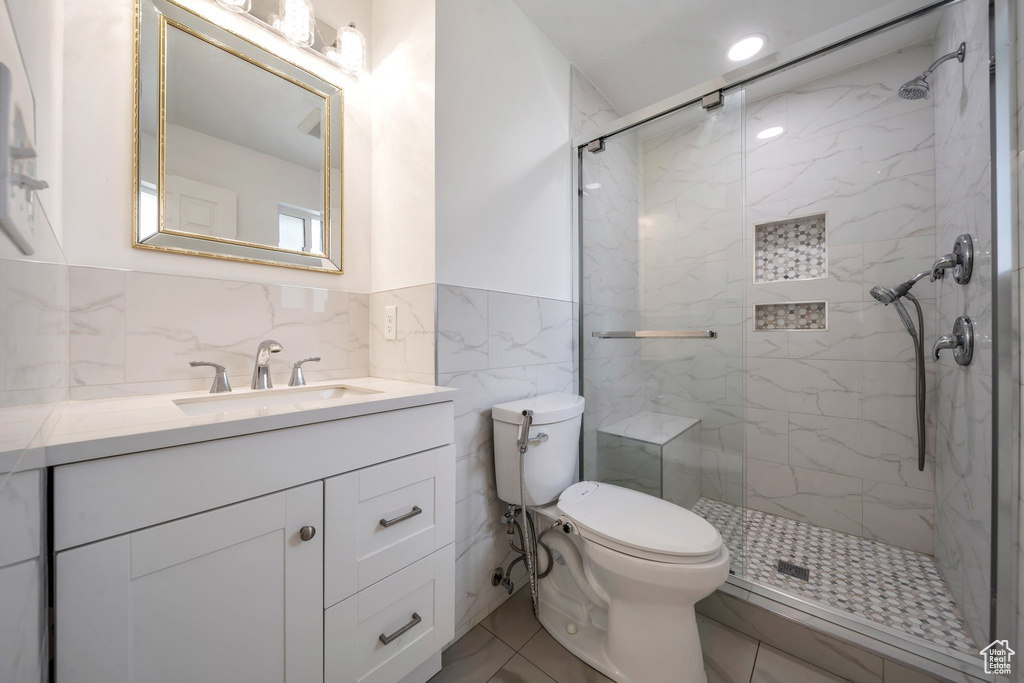 Full bath featuring a marble finish shower, vanity, tile walls, toilet, and wainscoting