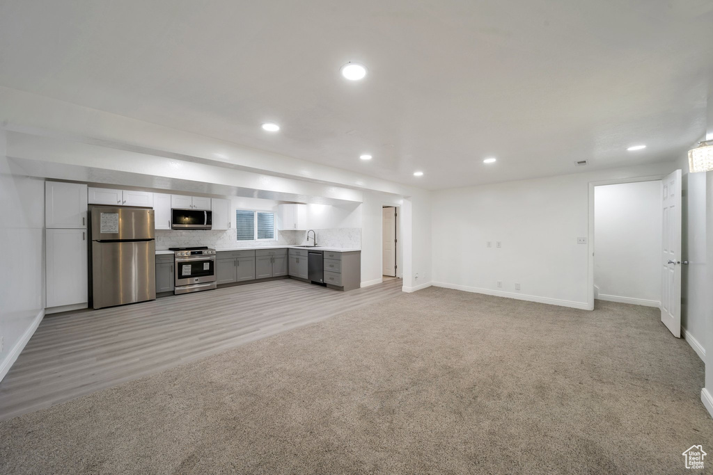 Unfurnished living room featuring baseboards, a sink, recessed lighting, light colored carpet, and light wood-style floors