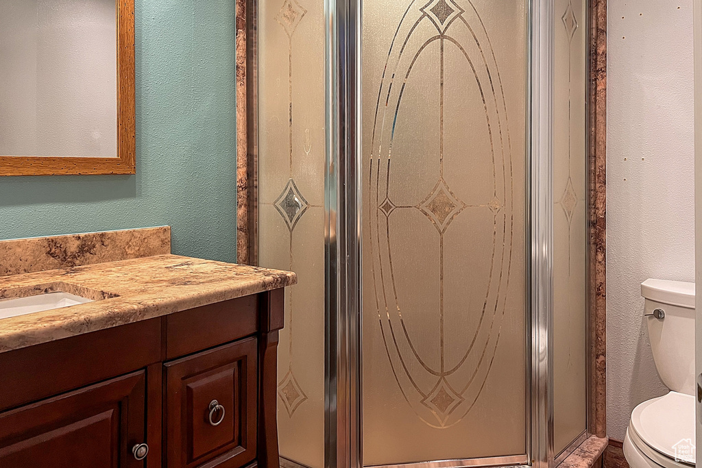 Full bathroom with vanity, a textured wall, a shower stall, and toilet