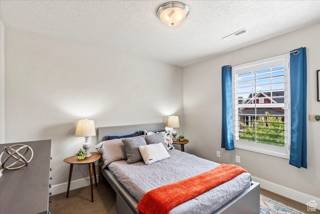 Bedroom featuring baseboards, carpet flooring, a textured ceiling, and visible vents