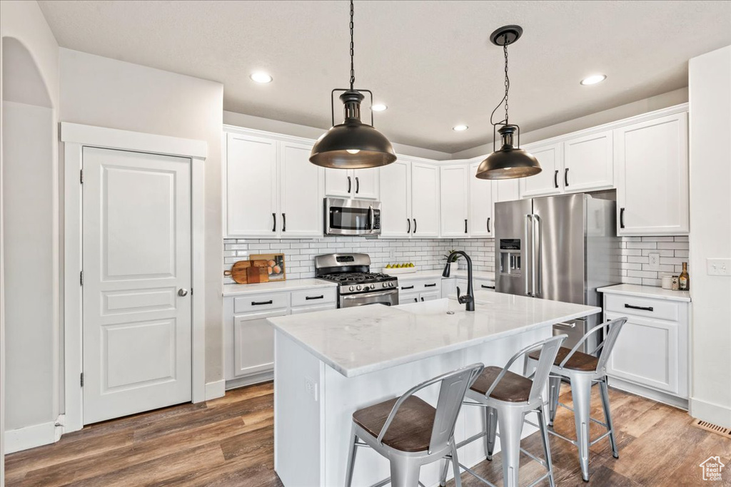 Kitchen featuring white cabinets, stainless steel appliances, a sink, and wood finished floors