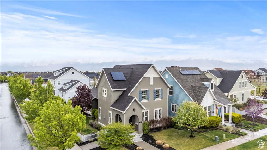 View of front of property with a residential view, fence, roof with shingles, stucco siding, and solar panels