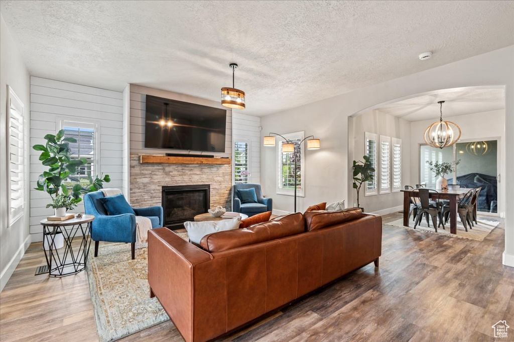 Living room with a textured ceiling, baseboards, a stone fireplace, and wood finished floors