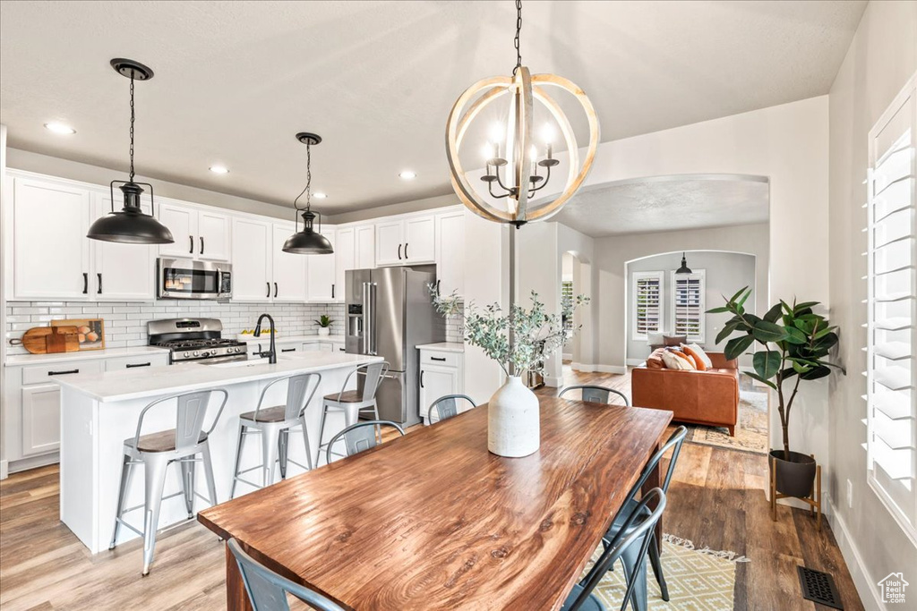 Dining area with arched walkways, baseboards, an inviting chandelier, and light wood-type flooring