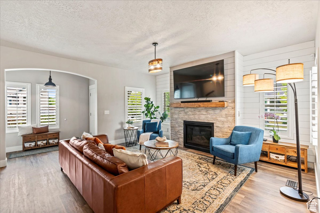 Living room with arched walkways, a textured ceiling, a stone fireplace, and wood finished floors