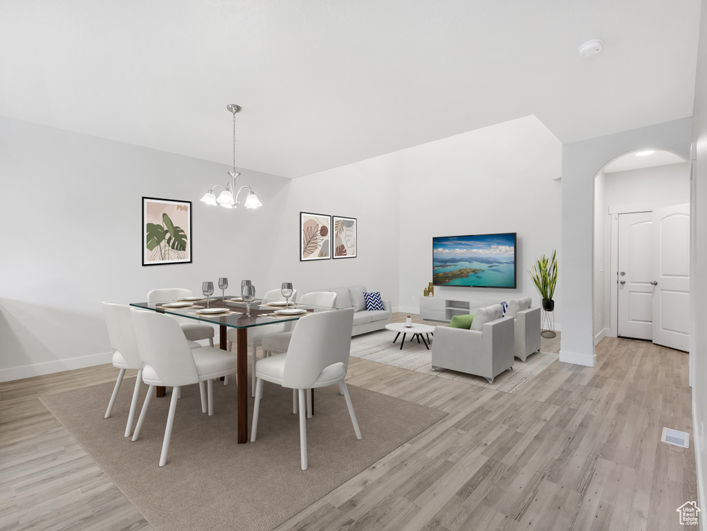 Dining space with light wood finished floors, arched walkways, baseboards, and an inviting chandelier