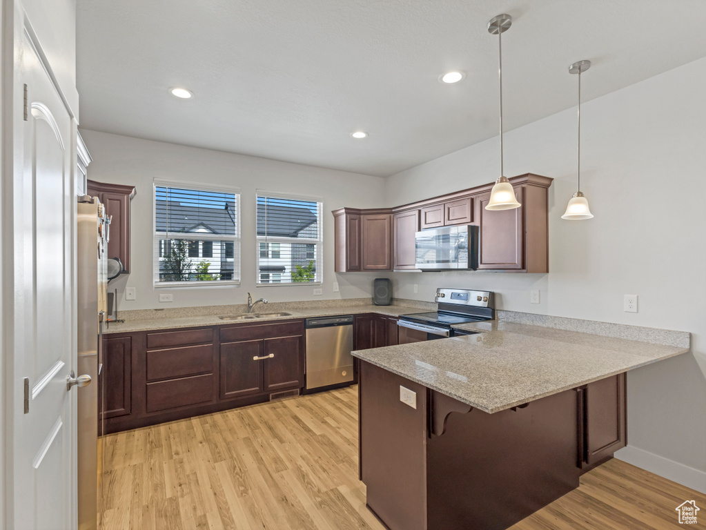 Kitchen featuring pendant lighting, light wood-style flooring, a sink, a peninsula, and stainless steel appliances