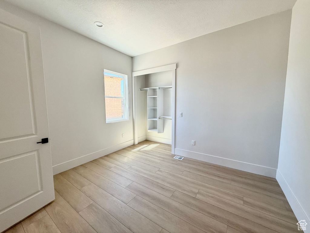 Unfurnished bedroom featuring light wood-type flooring, baseboards, and a textured ceiling