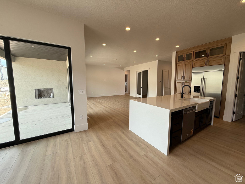 Kitchen with appliances with stainless steel finishes, light wood finished floors, brown cabinets, light countertops, and recessed lighting