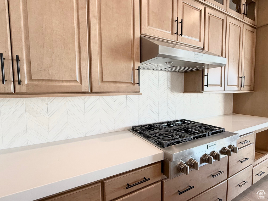 Kitchen with under cabinet range hood, stainless steel gas cooktop, tasteful backsplash, light countertops, and glass insert cabinets