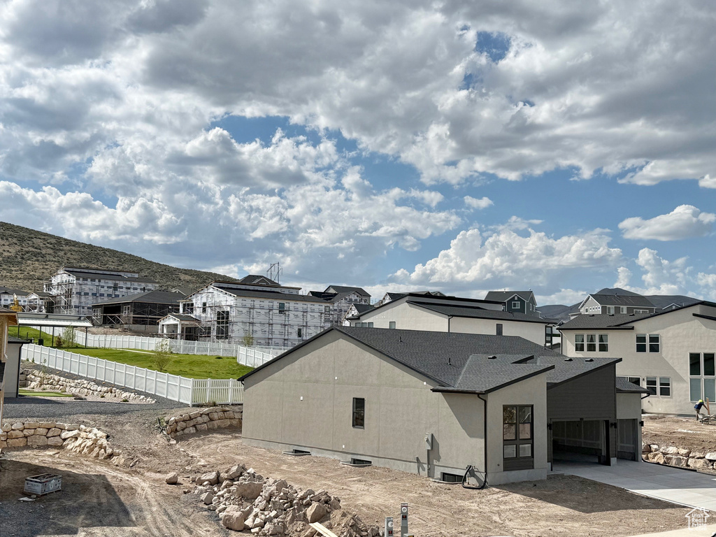 Back of house featuring fence, a mountain view, a residential view, concrete driveway, and a shingled roof