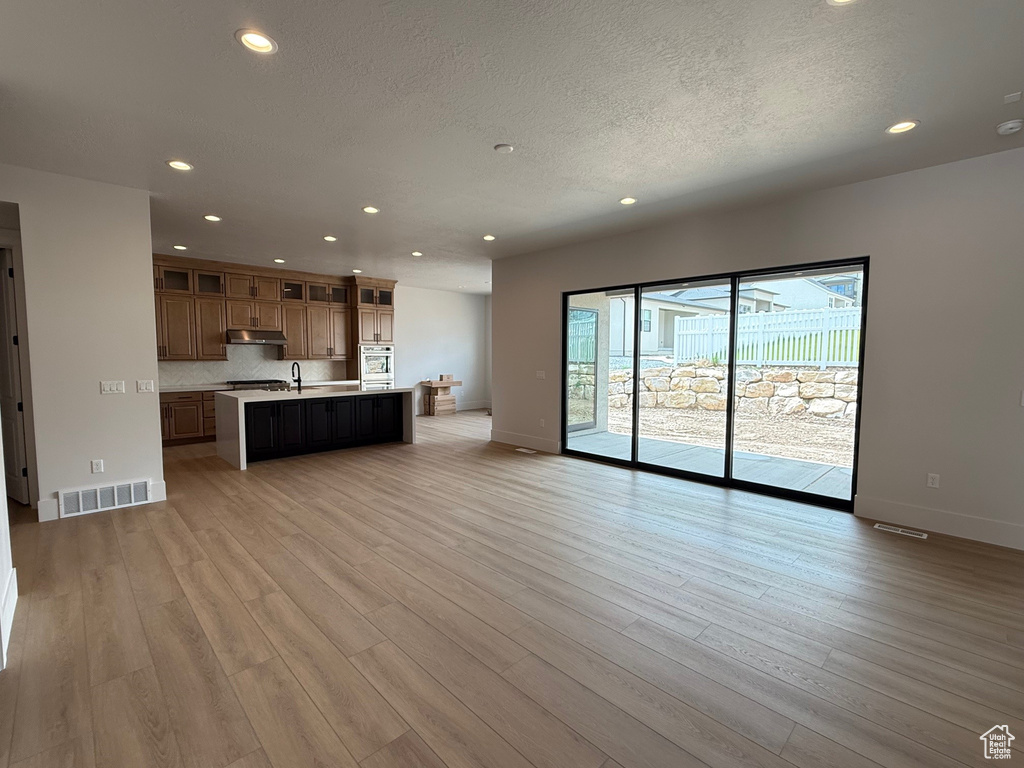 Unfurnished living room with recessed lighting, a textured ceiling, light wood finished floors, and baseboards
