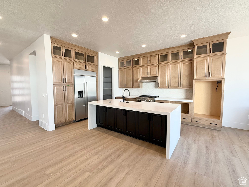 Kitchen with built in refrigerator, a kitchen island with sink, light wood-style floors, light countertops, and recessed lighting