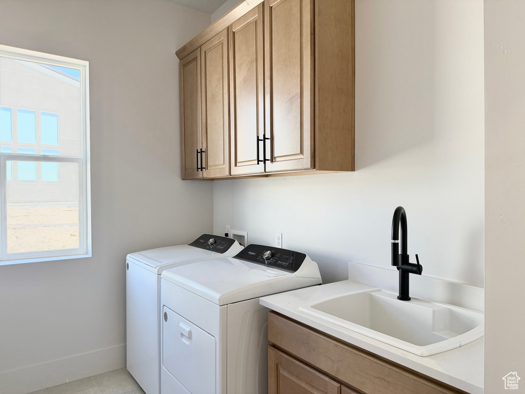 Clothes washing area featuring washer and dryer, cabinet space, healthy amount of natural light, and baseboards