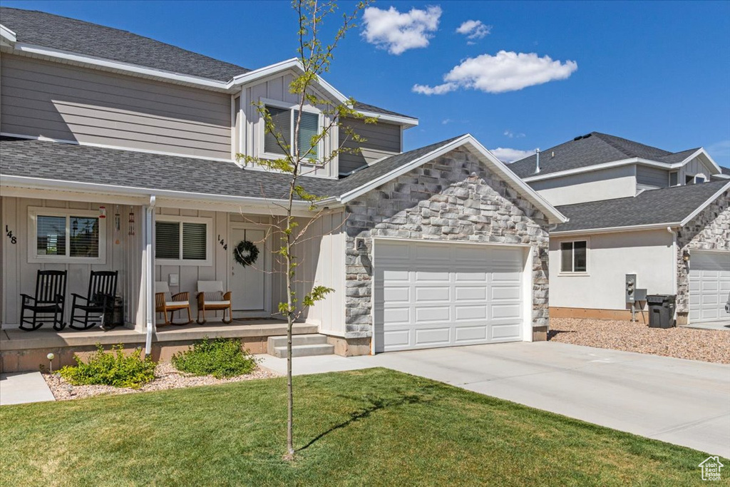 View of front of home with board and batten siding, covered porch, concrete driveway, and stone siding