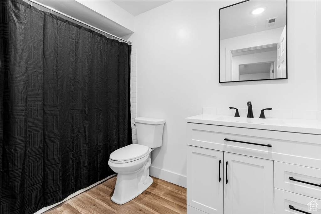 Full bathroom featuring wood finished floors, toilet, vanity, baseboards, and curtained shower