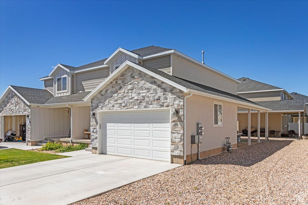 View of front of home with stone siding, a garage, concrete driveway, and roof with shingles