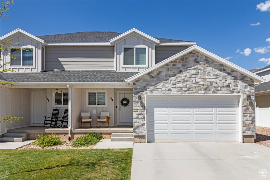 View of front of house with a porch, stone siding, concrete driveway, board and batten siding, and an attached garage