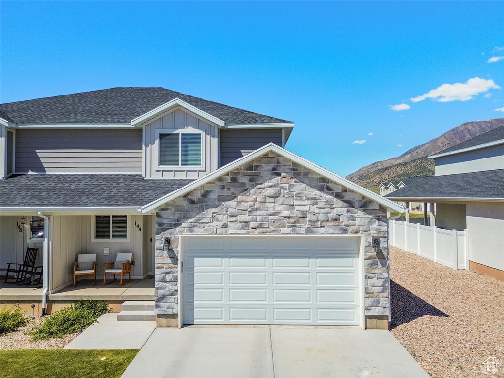 View of front facade featuring stone siding, a porch, concrete driveway, and fence