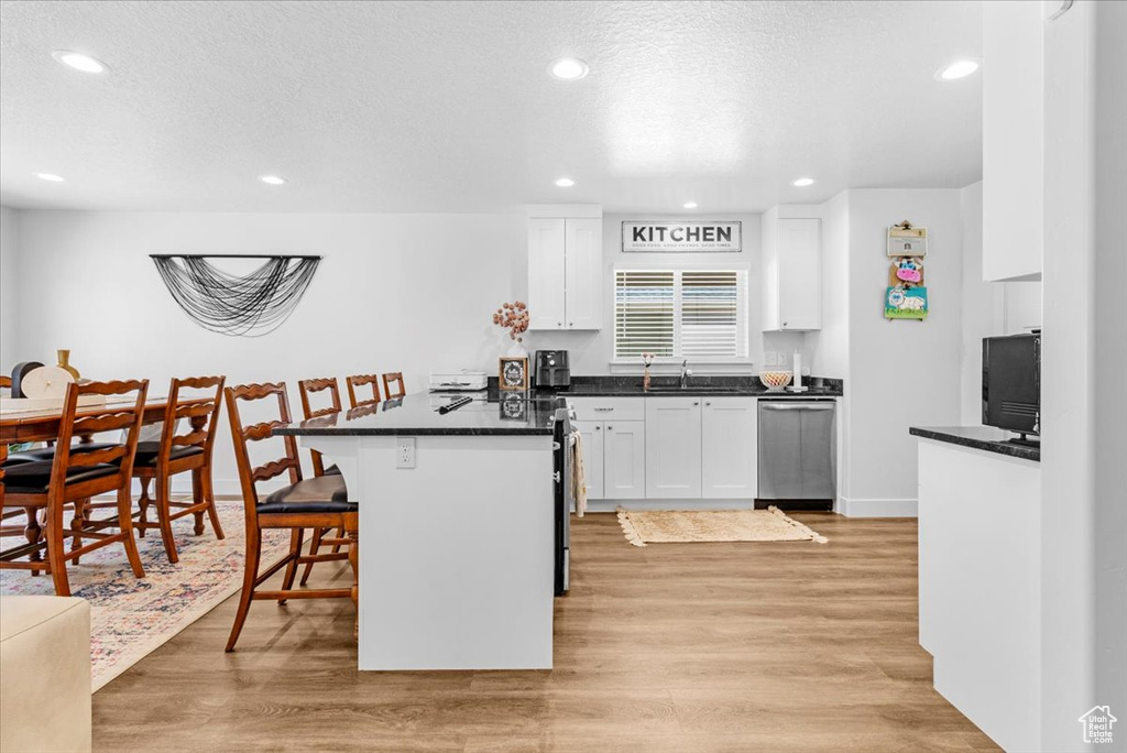 Kitchen featuring dishwasher, a breakfast bar area, white cabinetry, light wood finished floors, and recessed lighting