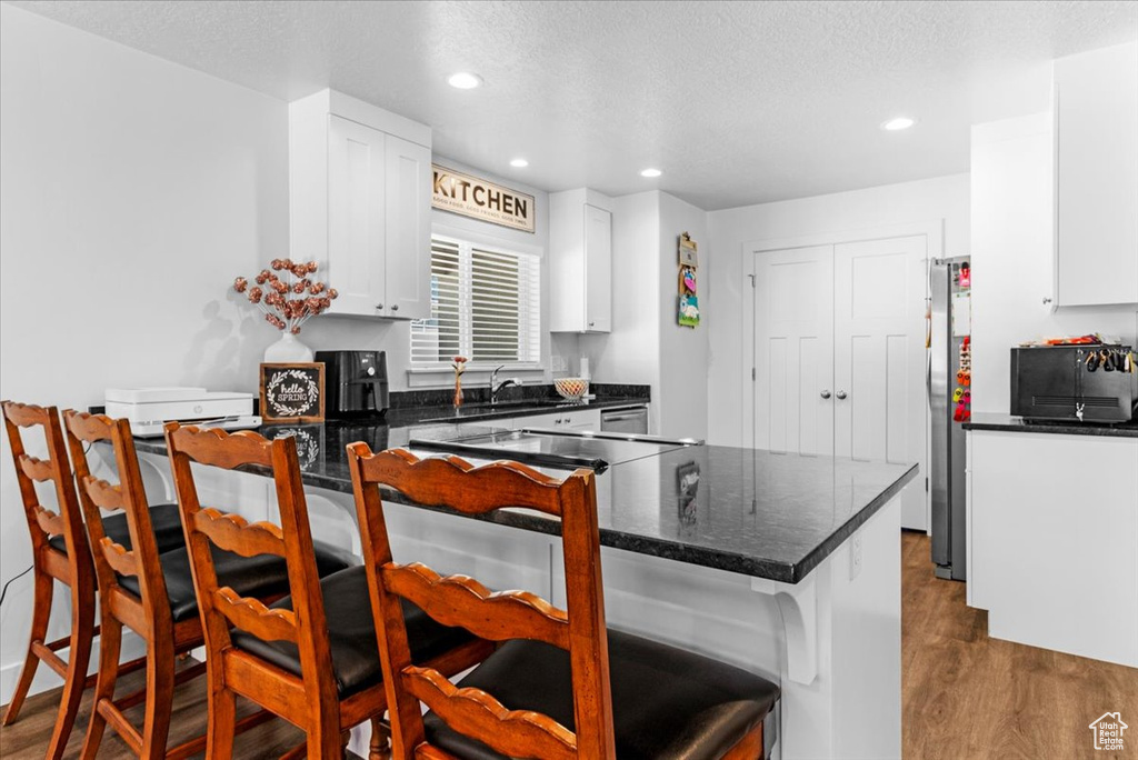 Kitchen with a breakfast bar, dark wood-style flooring, freestanding refrigerator, white cabinets, and recessed lighting