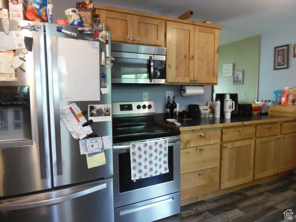 Kitchen with appliances with stainless steel finishes, dark wood-style floors, dark countertops, and light brown cabinetry
