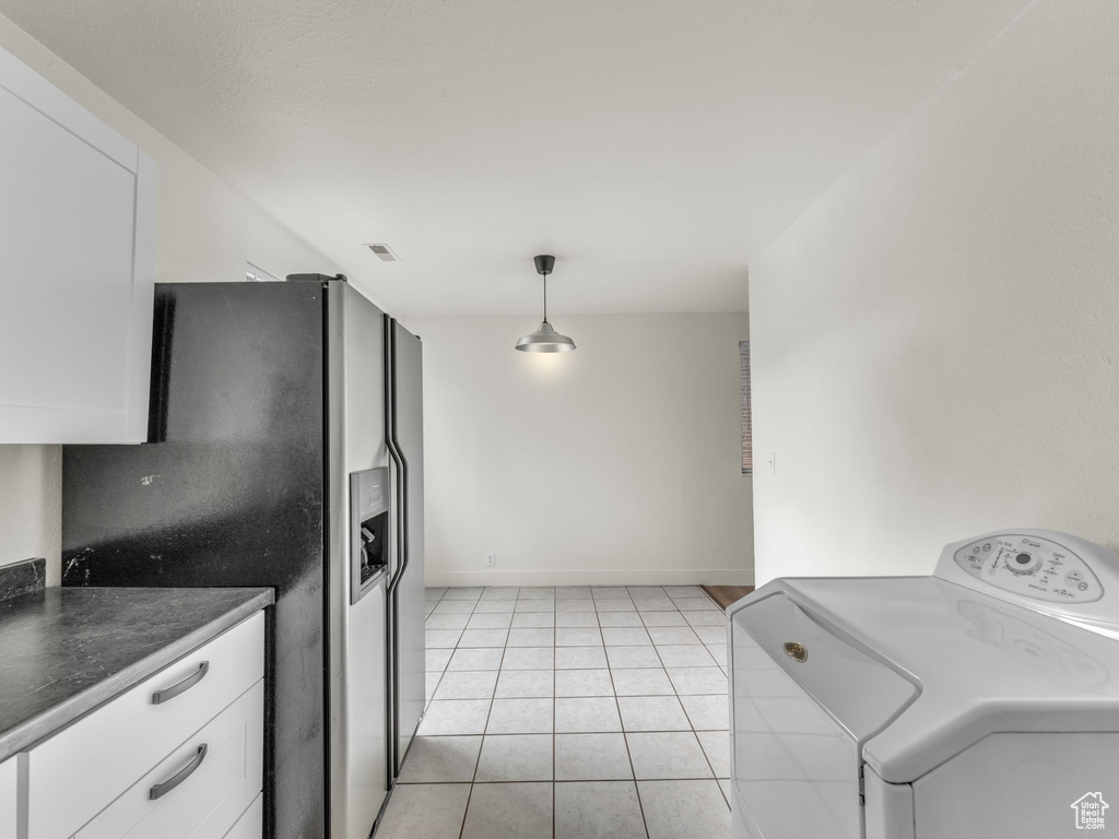 Kitchen featuring washer / clothes dryer, refrigerator with ice dispenser, white cabinetry, dark countertops, and light tile patterned flooring